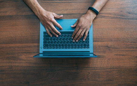 Mens hands in black electronic watches on the keyboard of a laptop against the background of a wooden tableの写真素材