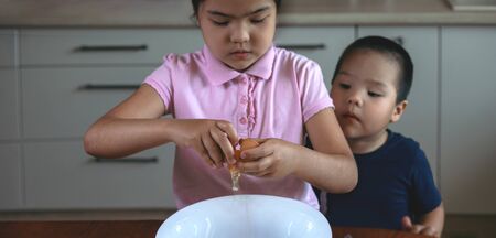 A girl and a boy break the egg in white bowl the kitchen at home. Stay at homeの写真素材
