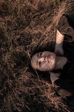 A beautiful Asian girl lies on the grass in the rays of the setting sun. Top view.の写真素材