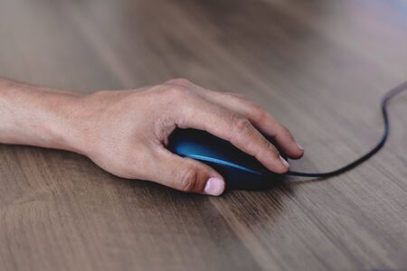A man uses a computer mouse on a wooden table. Side viewの写真素材