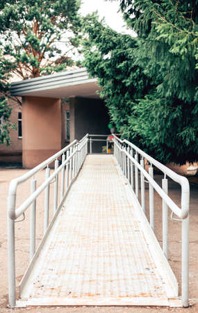 Metal ramp to support wheelchair users. Accessible environment for people with disabilities. Green branches of fir trees in the background.の写真素材