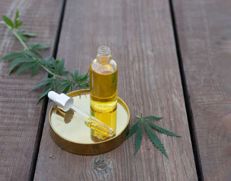 Glass bottle and dropper CBD OIL, THC tincture and cannabis leaf on wooden background. Laboratory Production of cosmetics with CBD oil. Top viewの写真素材