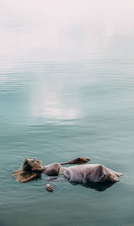 The girl lies peacefully with her eyes closed in the blue water. Copy space for text.の写真素材