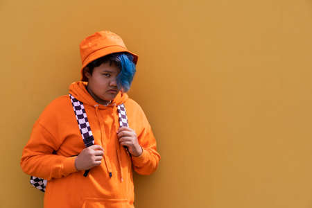 Back to school. Teenage girl with blue hair in an orange hoodie, a Panama hat with a backpack. High school kid.Education.の写真素材