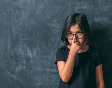 Back to school. Serious little girl adjusts his glasses near blackboard. Child from elementary school. Education.の写真素材