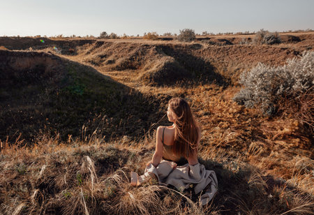 View from the back of a girl in a shirt sitting on a hill and admiring the beautiful view and...