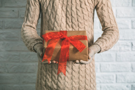 Girl in rubber gloves is holding a gift. Warm knitted sweater, the concept of holidays during the...