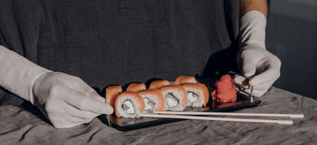 Hands in rubber gloves serve sushi on a black stand. Sushi menu. Japanese cuisine.の写真素材