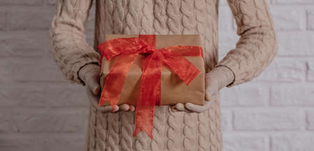 Girl in rubber gloves is holding a gift. Warm knitted sweater, the concept of holidays during the coronavirus pandemic. White brick wall backgroundの写真素材