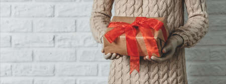 Girl in rubber gloves is holding a gift. Warm knitted sweater, the concept of holidays during the coronavirus pandemic. White brick wall backgroundの写真素材