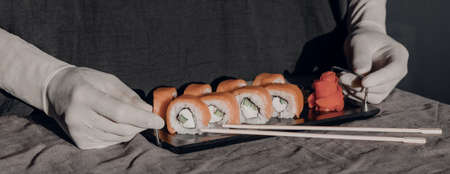 Hands in rubber gloves serve sushi on a black stand. Sushi menu. Japanese cuisine.の写真素材