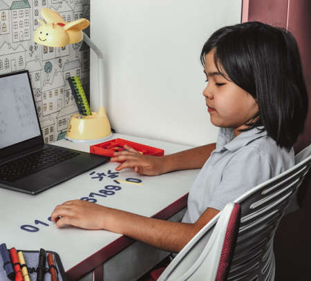 Asian schoolgirl studying homework math during her online lesson at home, video call zoom with laptop at home. New normal.Covid-19 coronavirus. Social distancing. Stay homeの写真素材