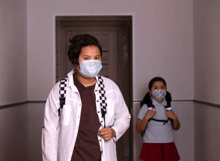 Teenager with face mask going back to school after covid-19 quarantine and lockdown. A child from elementary school in the background. Kids in masks for coronavirus prevention.の写真素材