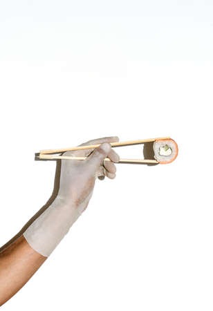 Hand in rubber glove hold sushi with chopstick on a white isolated background. Sushi menu. Japanese cuisine.の写真素材