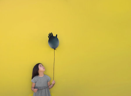 A sad girl holds an inflated glove in her hand instead of a balloon, it is her birthday during the coronovirus pandemic. Bannerの写真素材