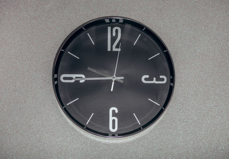 Black wall clock with a second hand hanging on the wall. A minimalist flat image of a plastic wall...