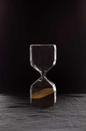 A sandglass, modern hourglass measuring the passing time in a countdown to a deadline, on a dark...
