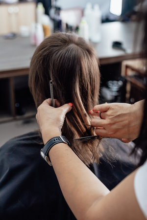 Woman getting a new haircut. Female hairstylist cutting her long black hair with scissors in hair salonの写真素材