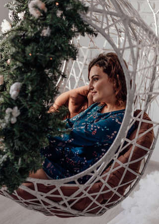 Christmas. Young girl Makeup. Healthy hair style. Elegant lady on a hanging chair decorated with New Years decorの写真素材