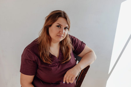 Attractive plus size girl sitting on chair, white background
