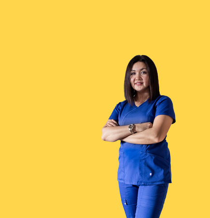 Full portrait of happy female doctor standing in uniform on yellow isolated background