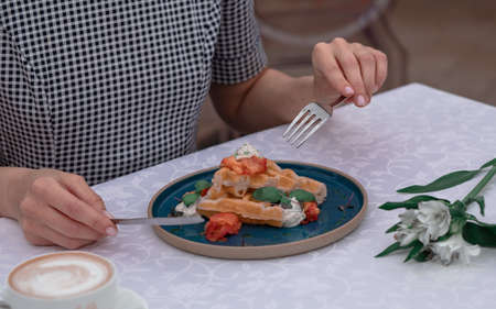 The girl is having breakfast with Belgian waffles with salmon pieces and sauce.の写真素材
