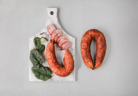 Classic salami on white chopping board with spinach on concrete background.