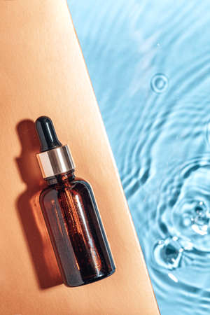 Cosmetic spa medical skincare, glass serum bottle with collagen on blue water background with waves. Advertising of medical product for anti-aging care, moisturizingの写真素材