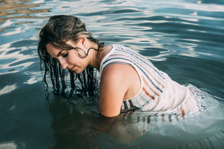 Elegant woman sit in the water. Sunset. The concept of unity with nature.の写真素材