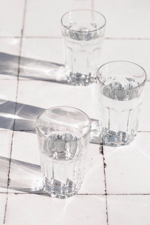 glass and sharp shadows stands on a white tiled table. top view of glassの写真素材