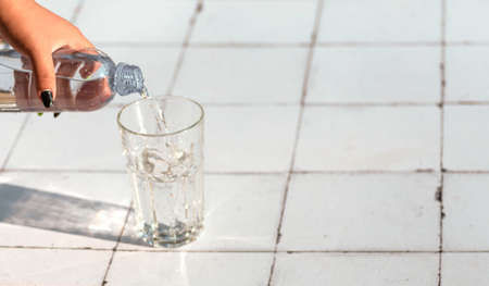 Pouring water from bottle into glass on a table made of white tilesの写真素材