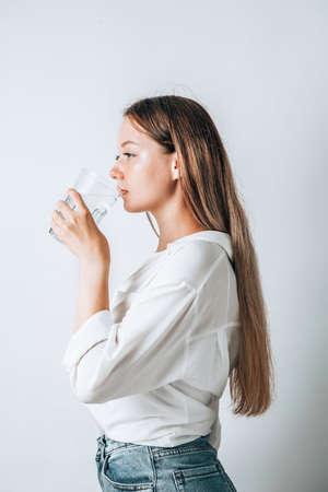 Asian girl with purple drinks water from a plastic bottle on a white isolated background. Generation Z. The concept of thirstの写真素材