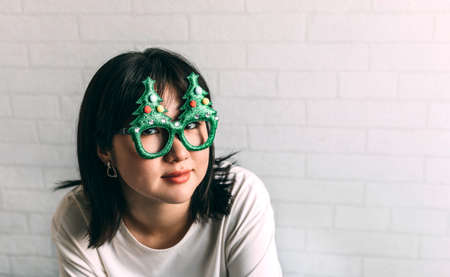 Stylish happy girl in festive glasses with christmas trees . Young hipster woman in cozy sweater.の写真素材