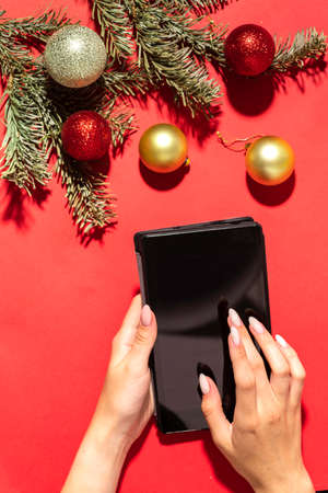 Hands using the tablet pc on Christmas background with fir branches, balls. Xmas and New Year theme. Flat lay, top view, space for textの写真素材