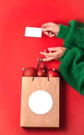 Xmas shopping concept. Womans hands holding a gift bag with balloons and a credit card on a red background,の写真素材
