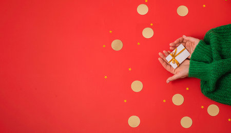 Gift card in womens palms on a red background with golden round and star-shaped confetti. Concept of...