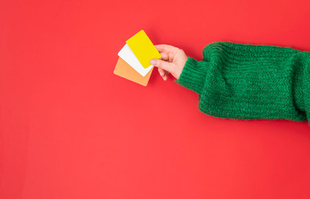 Christmas shopping concept. Flat lie hands in a green sweater with bonus, gift or credit card. Banner on a red backgroundの写真素材