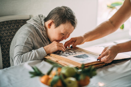 girl points a smiling elderly woman with Down syndrome to a photo in an old album.の写真素材