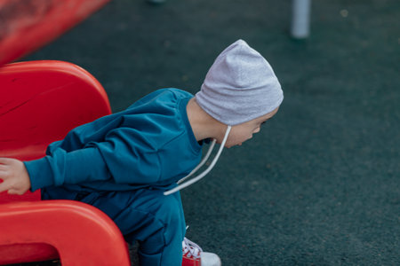 Cute Little boy with down syndrome in hat walks in the playground, rolling down the childrens slideの写真素材