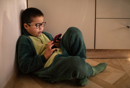 Closeup portrait of a boy who looks into the phone sitting on the floor, phone chargingの写真素材