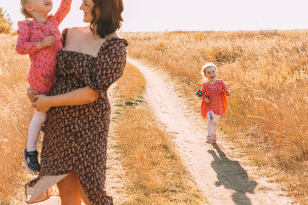 Mom with twins, holding a baby in her arms. The girl smiles and walks along the roadの写真素材