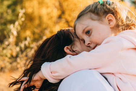Beautiful young woman and her charming little daughter are hugging and smiling outdoorsの写真素材