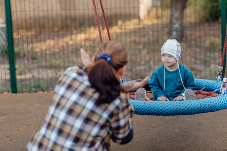 Cute Little boy with down syndrome in a funny hat with his mother, swinging on a swing, soap bubblesの写真素材