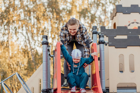 A boy, person with down syndrome walks in the park with his mother, going down the childrens slideの写真素材