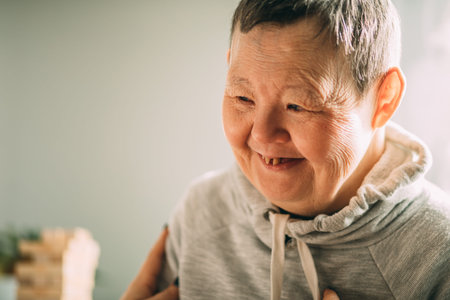 an elderly woman with Down syndrome, accompanied by an assistant who supports her, holds her handsの写真素材