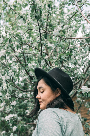 Beautiful asian plus size model wearing green dress enjoying smell of blooming spring tree outdoorの写真素材