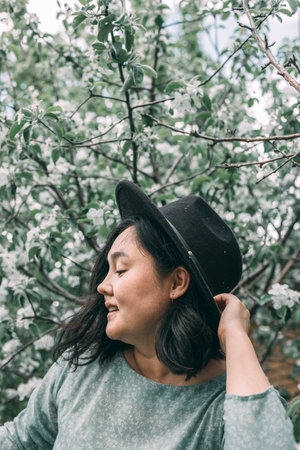 Beautiful asian plus size model wearing green dress enjoying smell of blooming spring tree outdoorの写真素材
