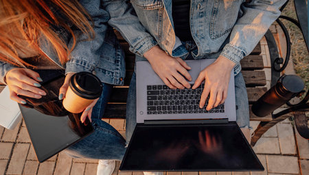 Close-up of the hands of a man and a woman with a laptop and tablet while working using laptop, sitting on the bench in parkの写真素材
