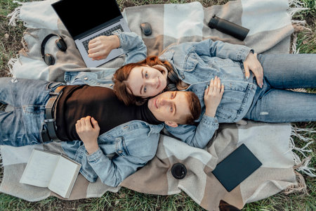 Pleased caucasian relaxed students lying near opened laptop, tries to have break after work in park. Work-Life-Balance concept.の写真素材