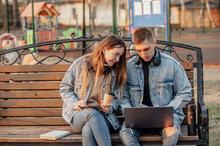 man and a woman with a laptop and tablet while working using laptop, sitting on the bench in park